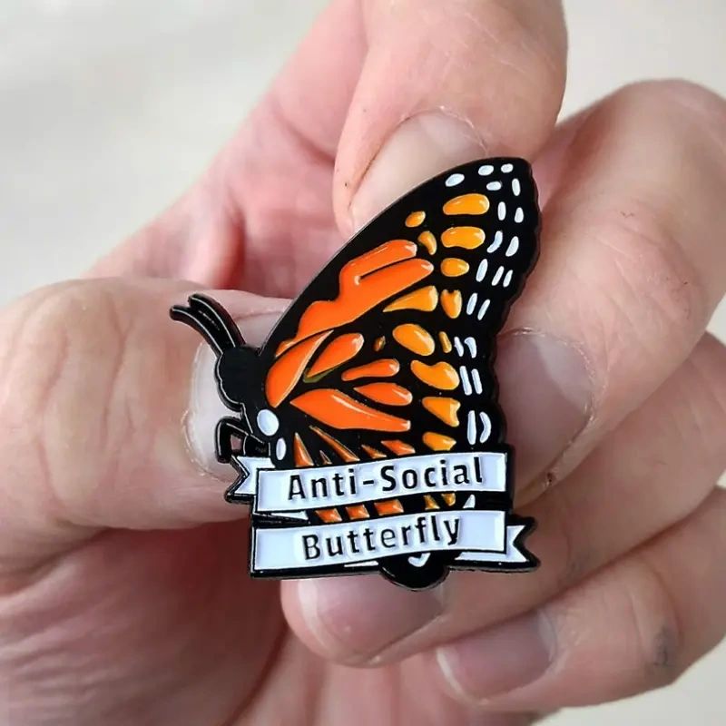 Hand holding anti-social butterfly pin.