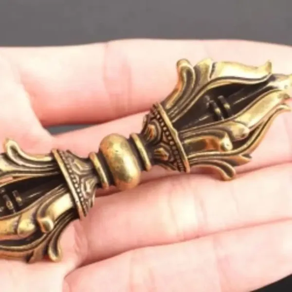 Gold-tone ornate ritual vajra held in hand.