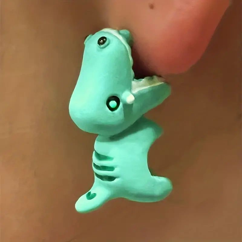 Green dinosaur earring on a person's ear.