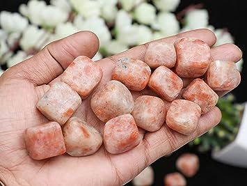 Hand holding a pile of sunstone tumbled stones.