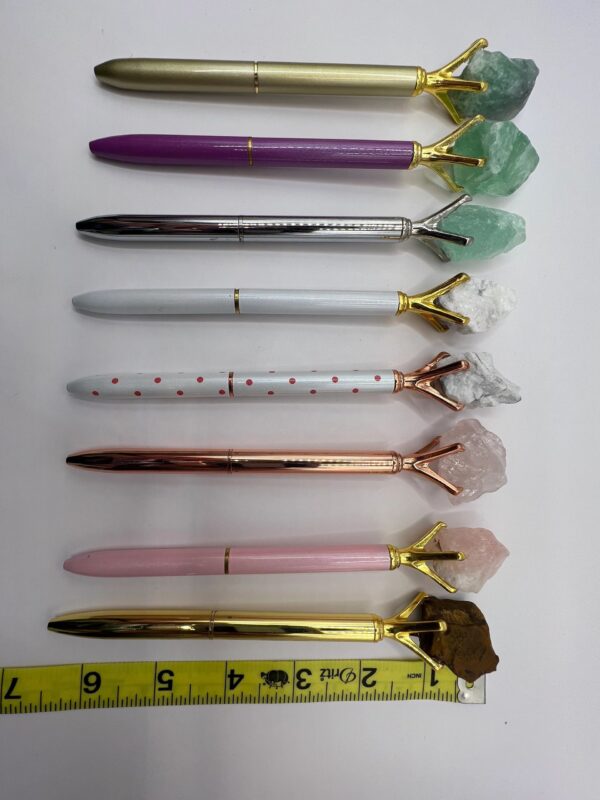 Seven crystal-topped pens on a white background.