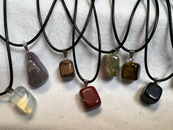 Seven gemstone pendants on black cords.