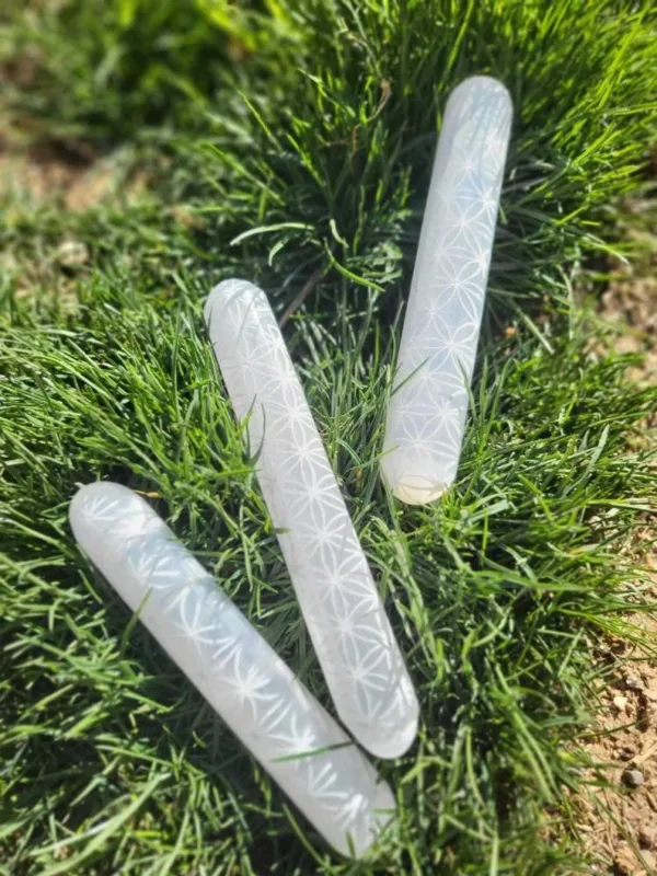 Three white selenite wands on grass.