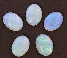 Five oval-shaped white opals on a dark surface.