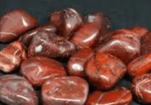 Red jasper tumbled stones on a dark background.